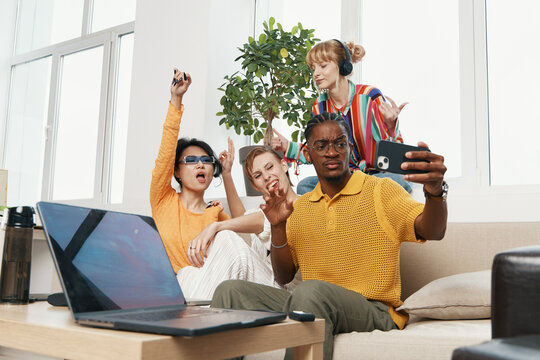 Young adult coworkers socializing in workplace, three friends including smiling man taking selfie, casual clothing and vibrant office atmosphere, Gen Z work culture.
