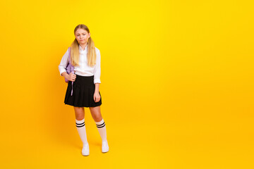 Young schoolgirl in a uniform holding a purple backpack against a bright yellow background for...