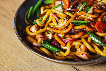 Stir fried noodles with vegetables. Colorful Asian dish in black bowl. Tasty mix of udon, meat and...