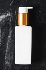 Minimal cosmetic bottle with pump on black stone background. White dispenser container for skincare or hygiene. Beauty product branding mockup. Modern clean design for lotion, soap or cream.
