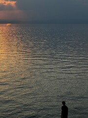 A person stands in silhouette on the shore of Thassos, gazing at the calm Aegean Sea under golden...