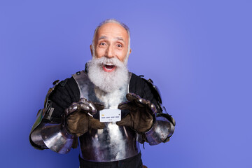 Laughing man in knight armor holding credit card in front of purple background
