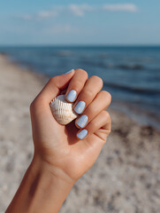 Beach-Inspired Nail Art on Woman's Hand Holding a Seashell by the Ocean