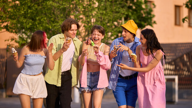 A diverse group of friends, gen z, savors ice cream and shares laughter outside on a sunny summer day. Concept of joy, friendship, and simple pleasures in life.