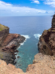 Photo of small bay on Madeira Island, featuring a high, rocky coastline and ocean waves crashing against large rocks.