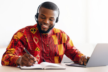 Online Learning. Cheerful Black Man In Traditional African Clothes Study With Laptop And Headset At...