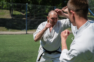 Karate fighter blocking high kick during outdoor training.