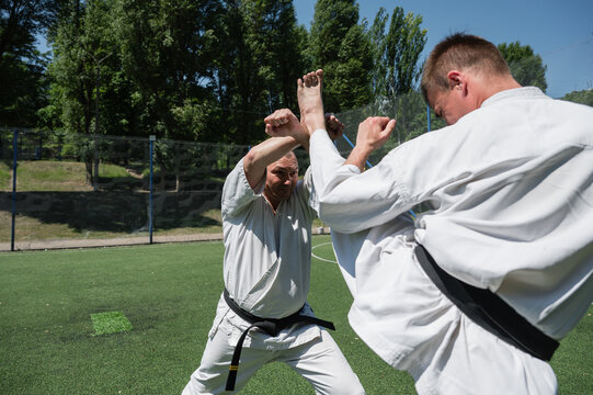 Karate fighter blocking high kick during outdoor training.
