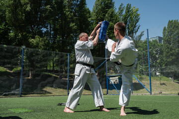 Karate student kicking training pad during outdoor session.