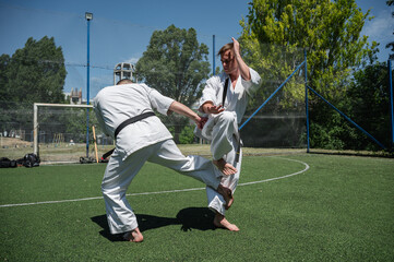 Obraz premium Karate practitioner performing leg sweep during outdoor sparring.