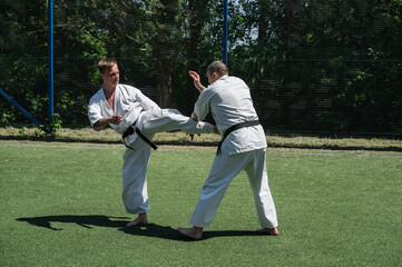 Man in white karate gi delivering a front kick to his sparring partner.