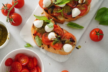 Bruschetta with Tomatoes and Mozzarella. Bruschetta with pesto sauce on white board. Mozzarella small ball with basil leaves on white table.