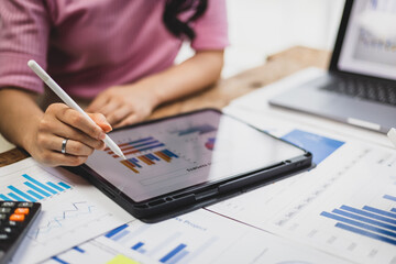 Businesswoman analyzing financial data on a tablet in her office, surrounded by paperwork and a...