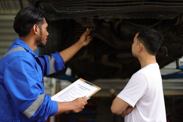 Mechanics in a car repair shop are discussing repairs to the underbody and suspension of an old car. Auto mechanic checking springs and shocks.