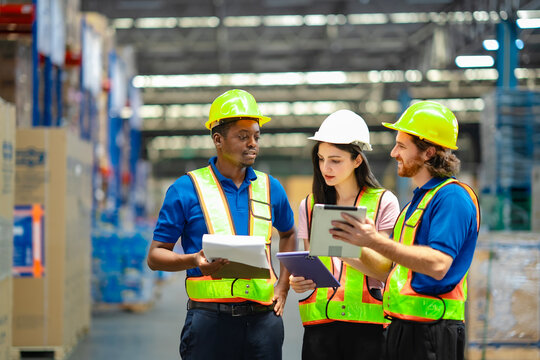 Warehouse professionals in reflective safety vests and helmets discussing inventory with digital tablet and clipboard. Emphasizing teamwork, workplace safety, and efficient supply chain operations.