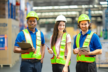 Diverse warehouse staff collaborating in factory setting, using tablet and clipboard for supply chain operations. Industrial teamwork, safety compliance, and logistics planning.