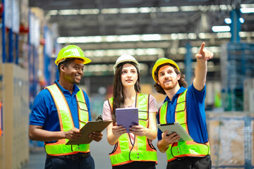 Diverse team of warehouse employees coordinating tasks and pointing forward. Teamwork, safety, and supply chain efficiency in distribution or storage facility.