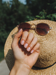 Natural nude pink manicure with straw sunhat in outdoor summer setting