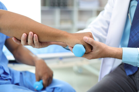 Doctor in hospital is practicing physical therapy on the arm of a male patient who is lifting a dumbbell.
