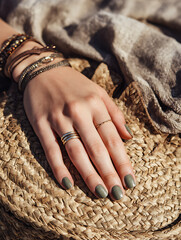 Earthy green nail polish on hand with boho jewelry resting on woven straw hat