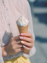 Colorful pastel nails holding vanilla ice cream cone with sprinkles on a sunny day