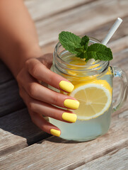 Yellow Summer Manicure with Lemon Drink on Wooden Table