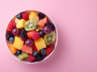 colorful fruit salad in a bowl on pink background, top view, flat lay with copy space