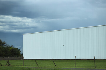 
White industrial warehouse in the countryside under a cloudy sky