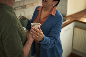 Senior couple sharing moment while drinking coffee in cozy kitchen. Both are smiling and holding coffee mugs, enjoying conversation and presence