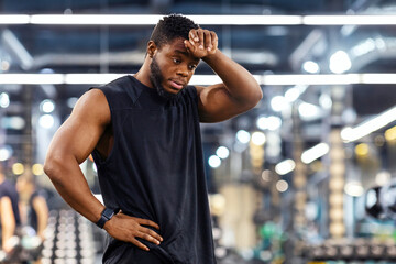 Exhausted black sportsman cleaning sweat from his forehead while having workout, copy space. Tired...