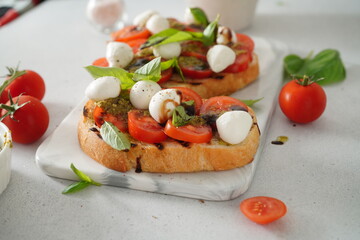 Bruschetta with Tomatoes and Mozzarella. Bruschetta with pesto sauce on white board. Mozzarella small ball with basil leaves on white table.