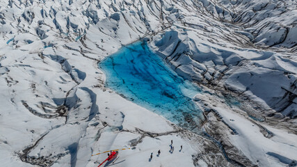 aerial landscape view of a massive Glacier with rugged surface with a red Helicopters on surface...