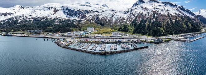 wide angle panoramic aerial landscape view of Whittier Cityscape with Harbor and Port located at head of Passage Canal in Alaska, USA, with snow covered mountain landscape in background 
