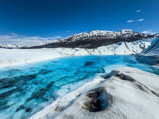 close up of a bright blue Glacier lake surrounded by Glacier with rugged surface and snow covered...