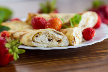 Delicious pancakes with strawberries and soft cottage cheese on a wooden table