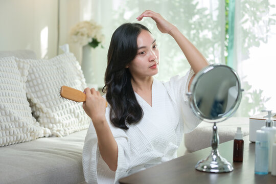 Smiling young woman in white robe brushing her hair and smiling in front of a mirror.