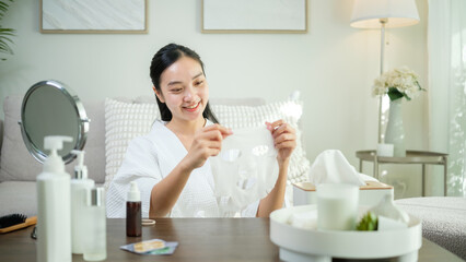 Young woman in a bathrobe applying a sheet mask while enjoying a skincare routine at home.