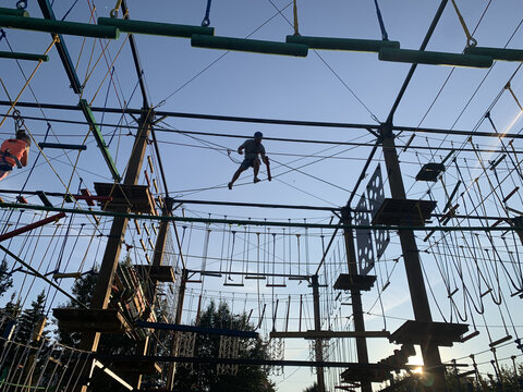 Adult man climbing and balancing on high ropes obstacle course in adventure park. Outdoor summer activity, sports entertainment, zipline and rope bridges. Active recreation and extreme training. - Powered by Adobe