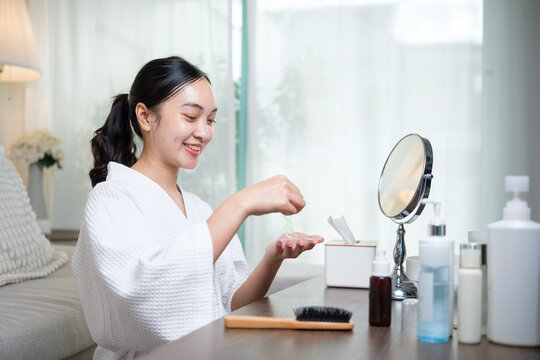 Smiling woman applying under eye patch during morning skincare routine at home. Self care concept.