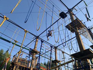 Adult man climbing and balancing on high ropes obstacle course in adventure park. Outdoor summer activity, sports entertainment, zipline and rope bridges. Active recreation and extreme training.