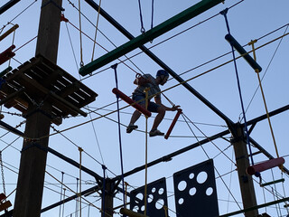 Adult man climbing and balancing on high ropes obstacle course in adventure park. Outdoor summer activity, sports entertainment, zipline and rope bridges. Active recreation and extreme training.