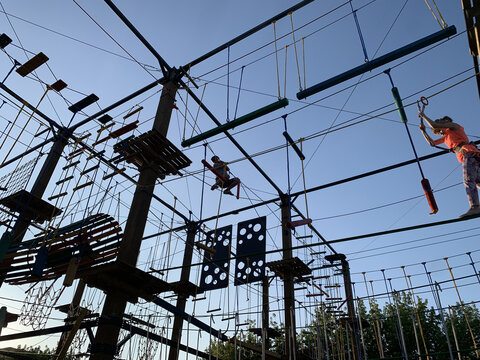 Adult man climbing and balancing on high ropes obstacle course in adventure park. Outdoor summer activity, sports entertainment, zipline and rope bridges. Active recreation and extreme training.