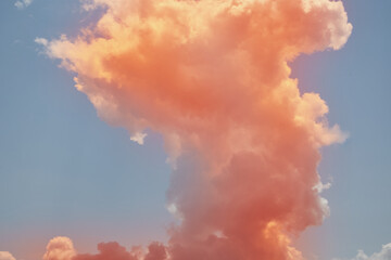 Large vertical orange cloud like an explosion in the blue sky close-up, orange cloud close-up.