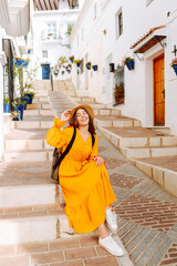 Beautiful tourist in bright dress enjoying trip to new city posing against white houses. Young...