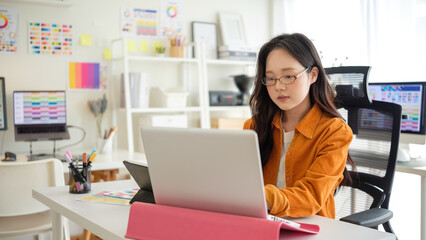 Young female graphic designer working on a creative project at her desk with color palettes and...