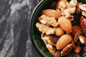 Mixed nuts in black bowl. Healthy snack with almonds and walnuts. Natural source of protein and fat. Fresh dry food on dark kitchen background. Diet and nutrition concept.