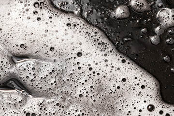 White foam on black background. Abstract cleaning texture with soap bubbles. Close-up of detergent...