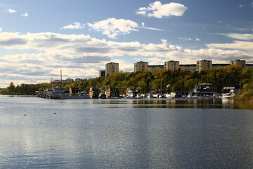 Fototapeta premium Residential buildings of Stockholm across water with tree-lined shoreline under a partly cloudy spring sky