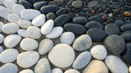 Smooth white and black pebbles arranged in gradient pattern on sandy surface, creating natural and calming aesthetic
