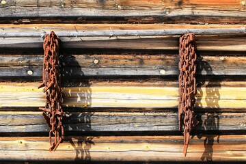 Rusted chains hang from a wooden cabin wall, casting long shadows in the morning light